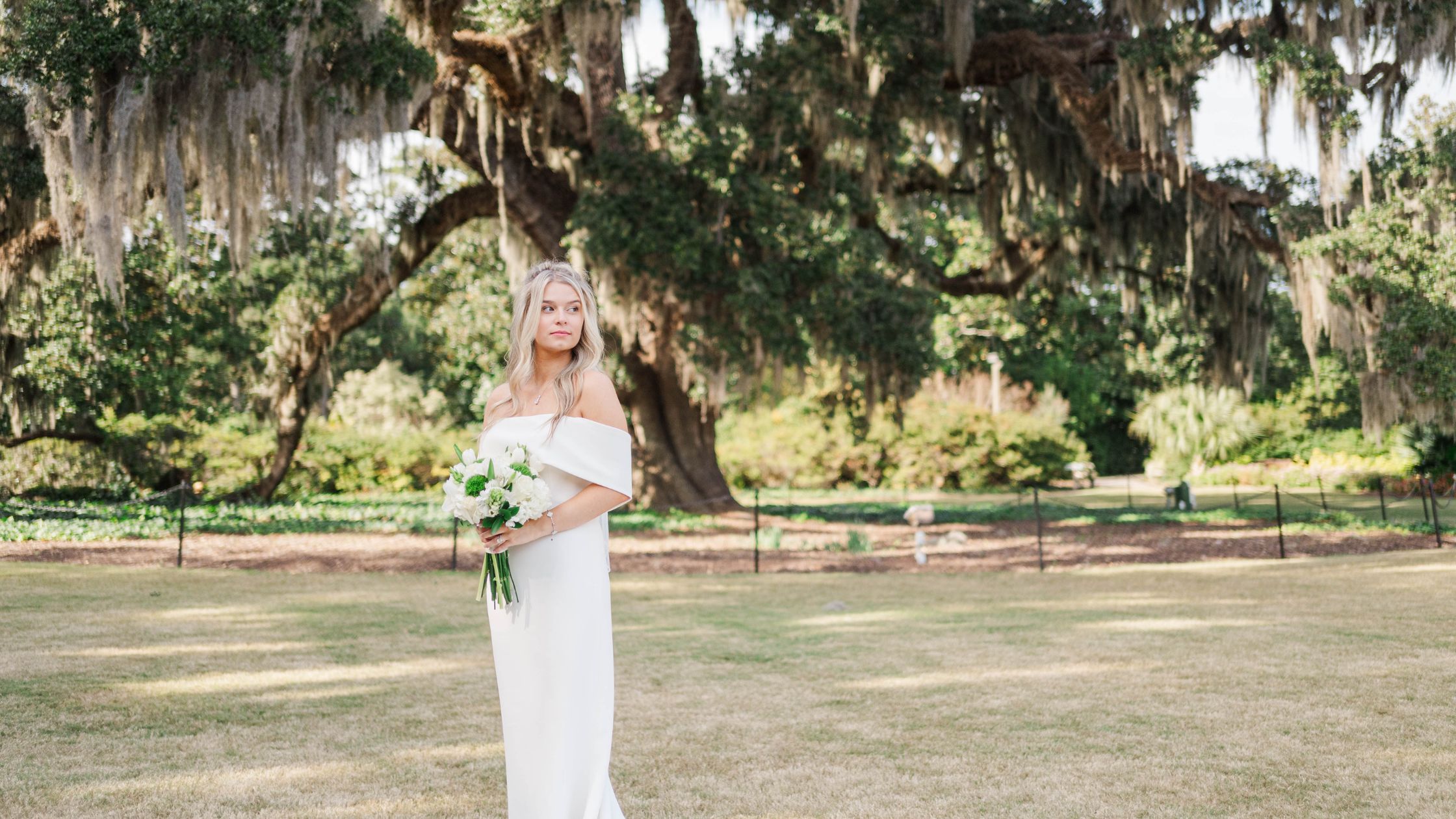 bride on her wedding day in raleigh, nc looking to the side in front of a large oak tree holding her bouquet of flowers